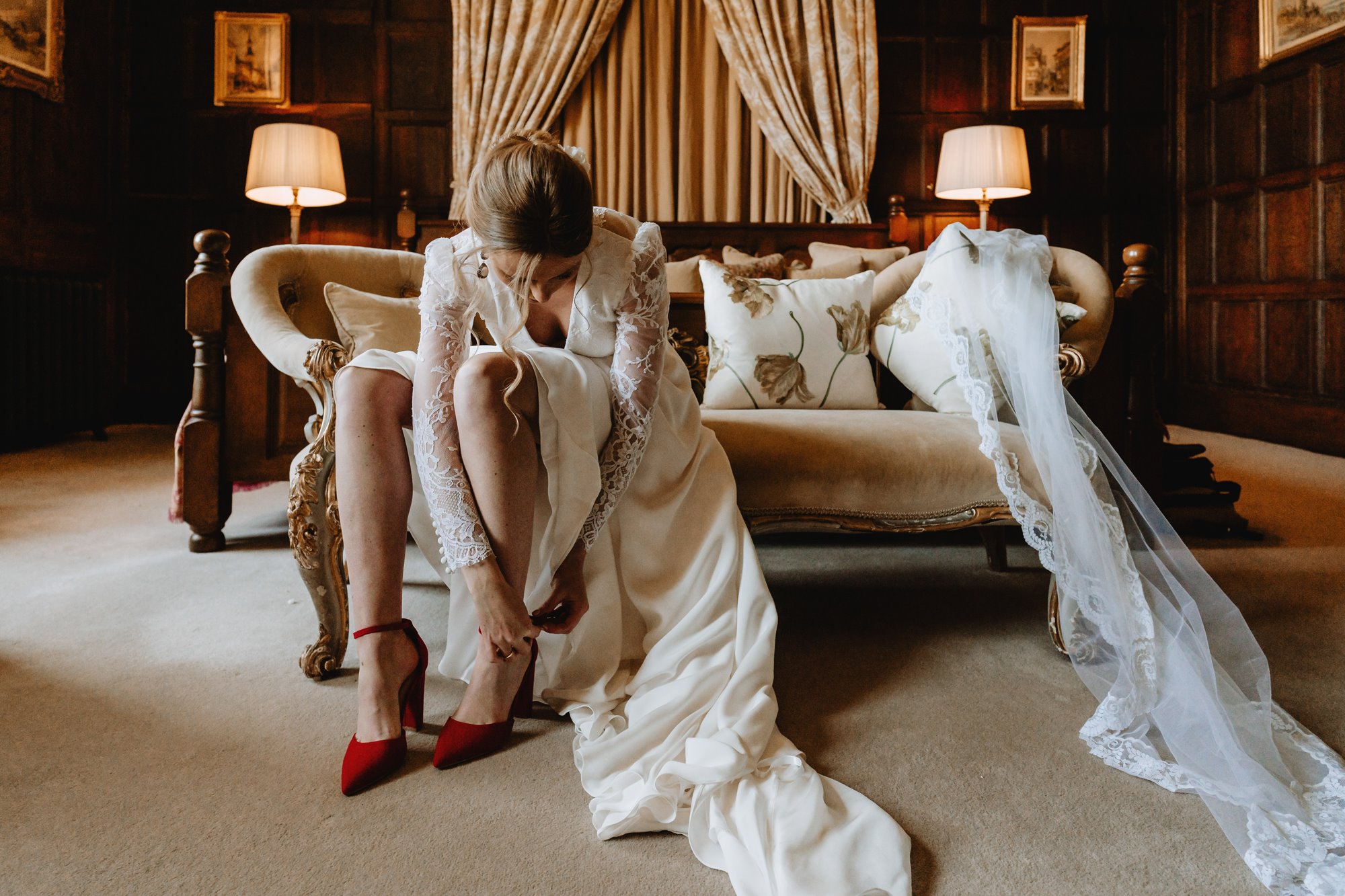 Stunning bride putting on bright red high heels as she gets ready for her wedding