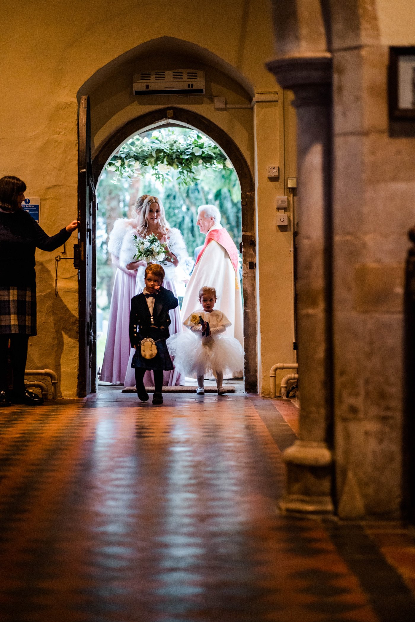 Flower girl and page boy enter the church through beautiful door vicar and bride follow