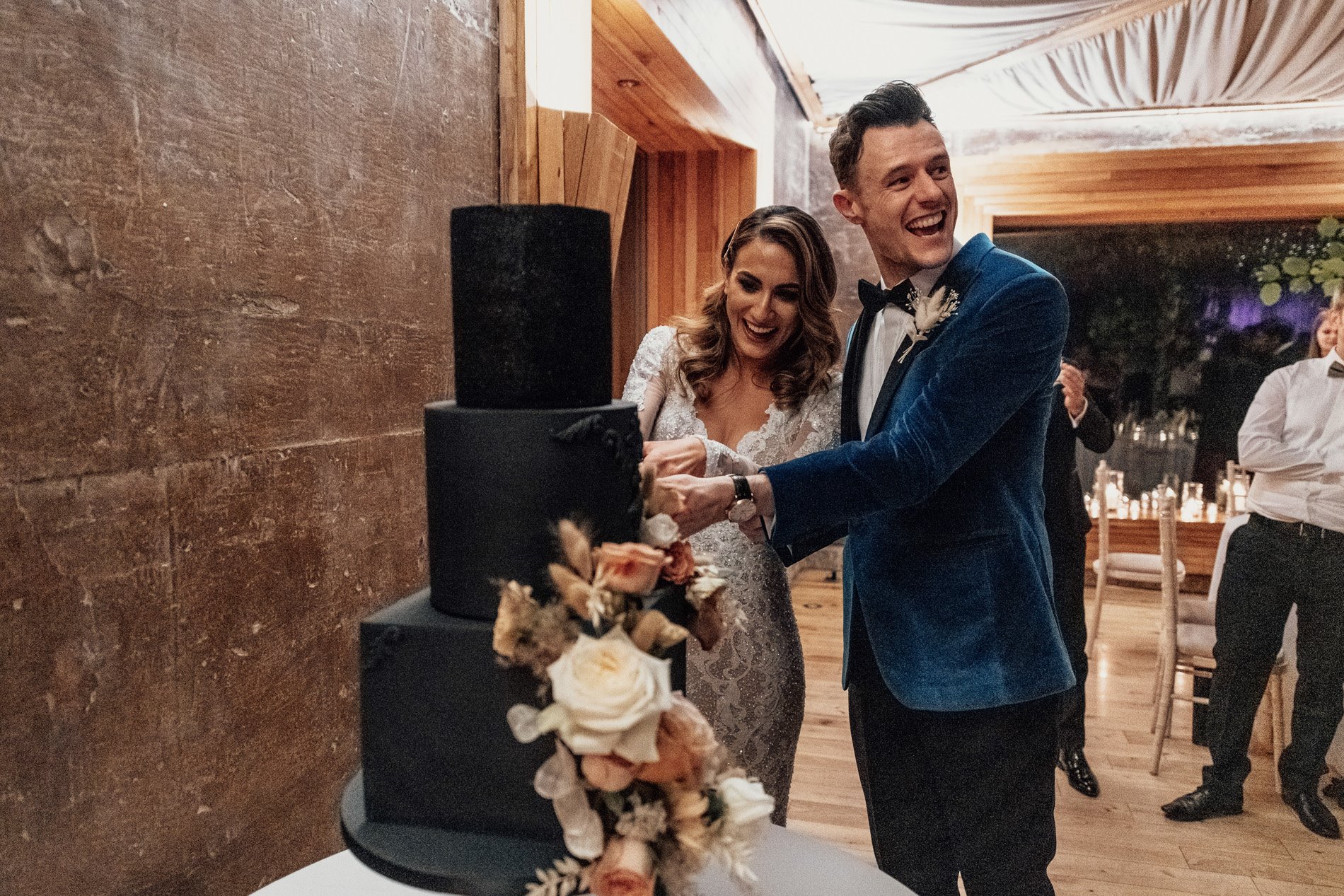 Couple cut their black wedding cake smiling in The Gillyflower Cotswolds