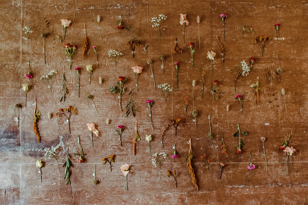 Autumn wedding flower wall with single flowers individually hung on earthy walls of the eco wedding reception
