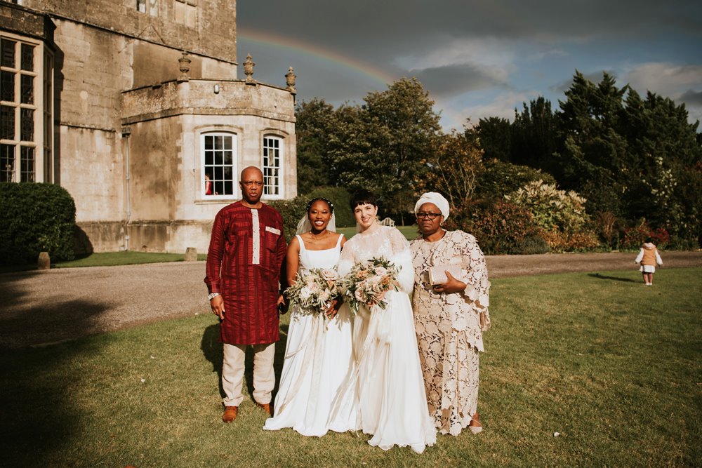 Rainbow shines in the sky over lesbian couple and their family on their multicultural wedding day in the cotswolds