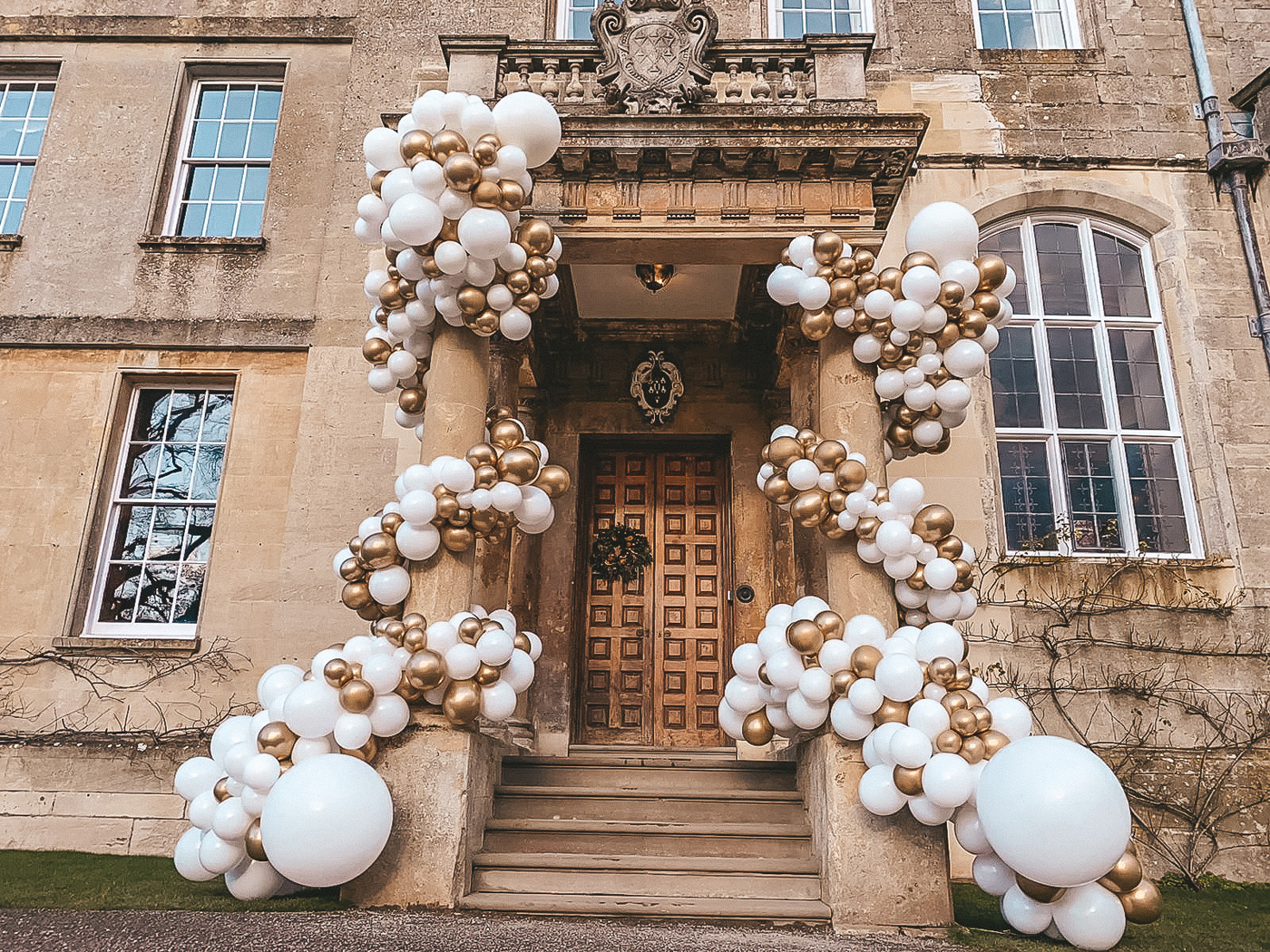 Wedding balloon installation in gold and white on the steps of a stately home for a wedding fair in Gloucestershire