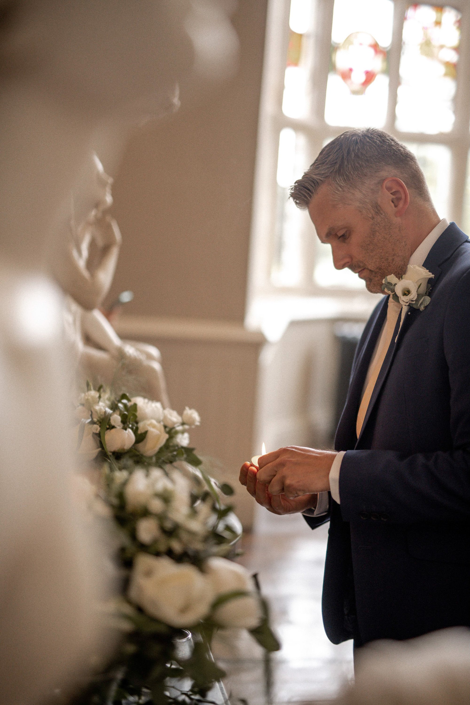 Unity candle ceremony groom lighting candle next to angel statue in stately home elmore court