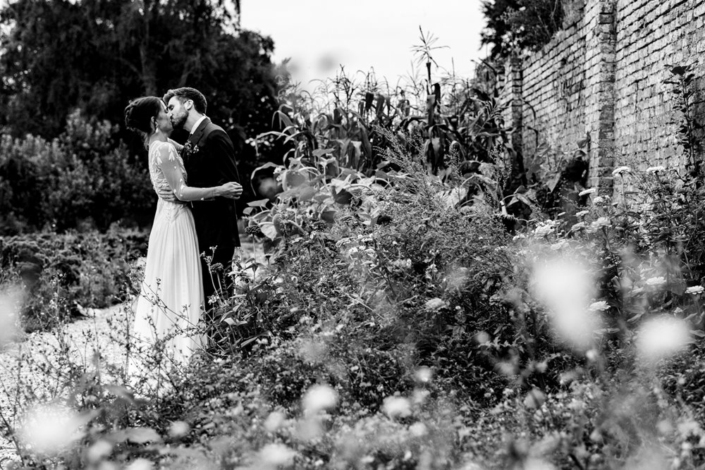 black and white shot of couple kissing amongst the flowers in the walled garden