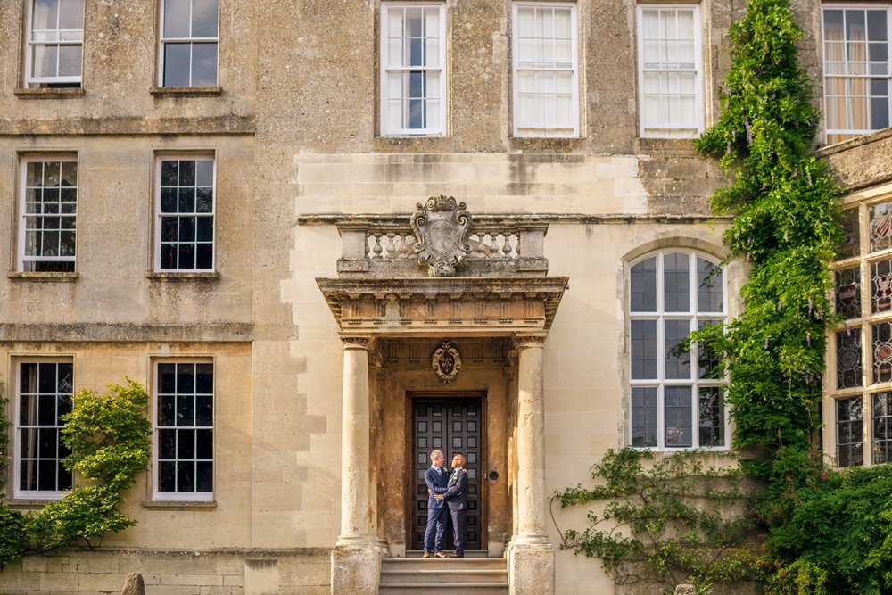 gay couple embrace on the steps of mansion elmore court in the cotswolds