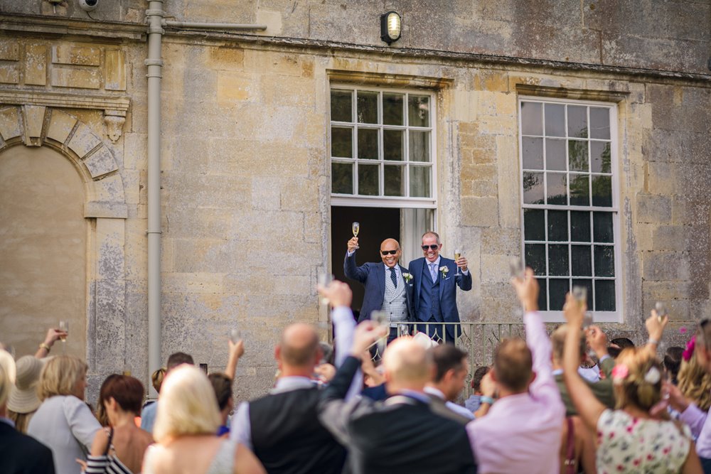 Two grooms toasted by their many guests outdoors at mansion house