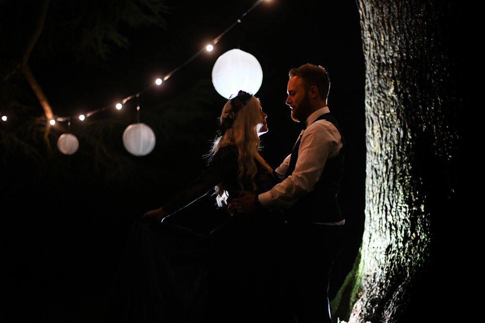 Magical wedding photoshoot with bride in black dress and autumn flower crown and lanterns on trees for halloween wedding