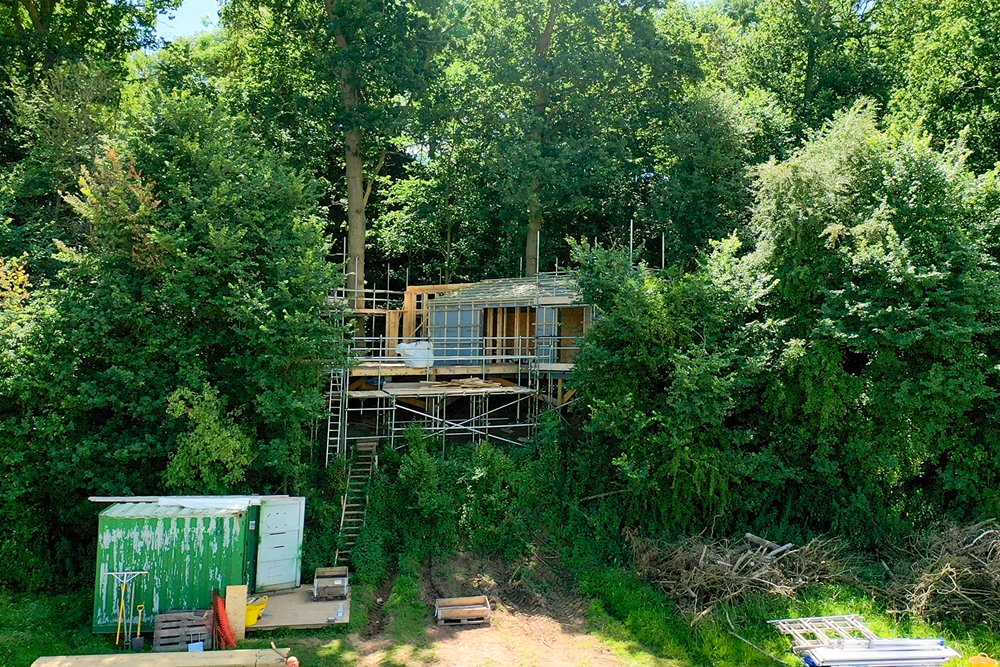 A treehouse in construction, sitting on stilts on the border of a beautiful woodland