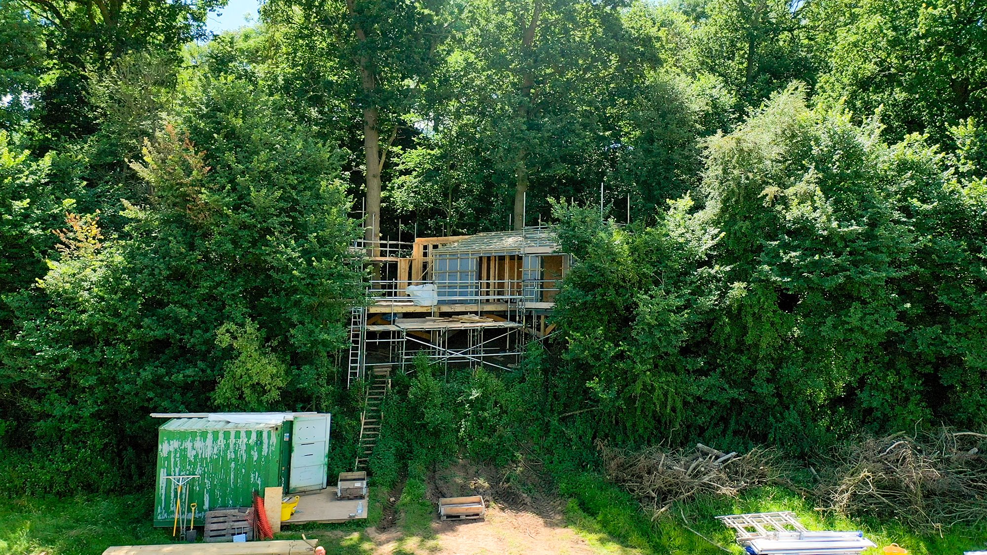 A treehouse in construction, sitting on stilts on the border of a beautiful woodland