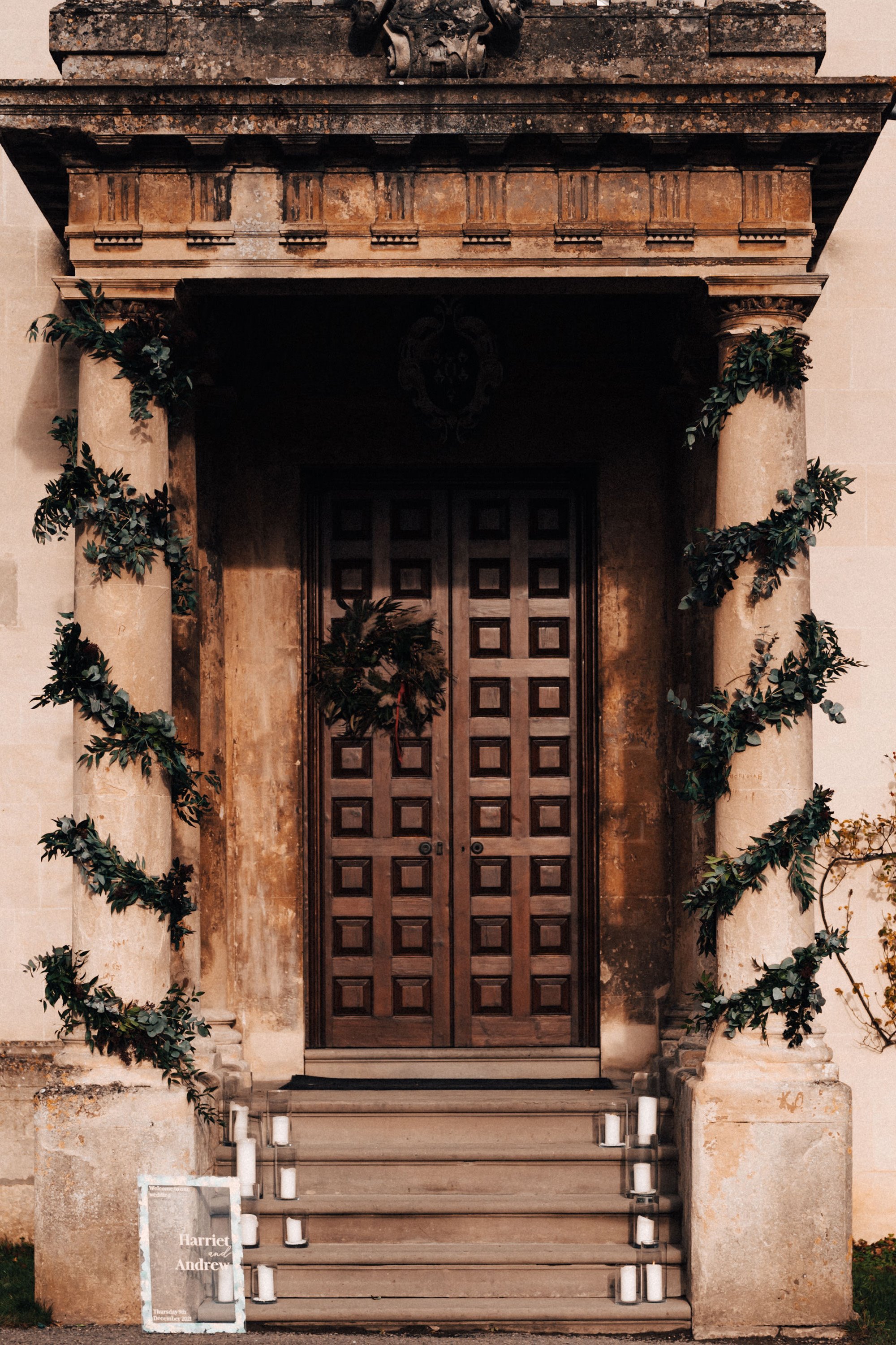 Steps of stately home decorated with candles and greenery and christmas wreath on door for a winter wedding in the cotswolds