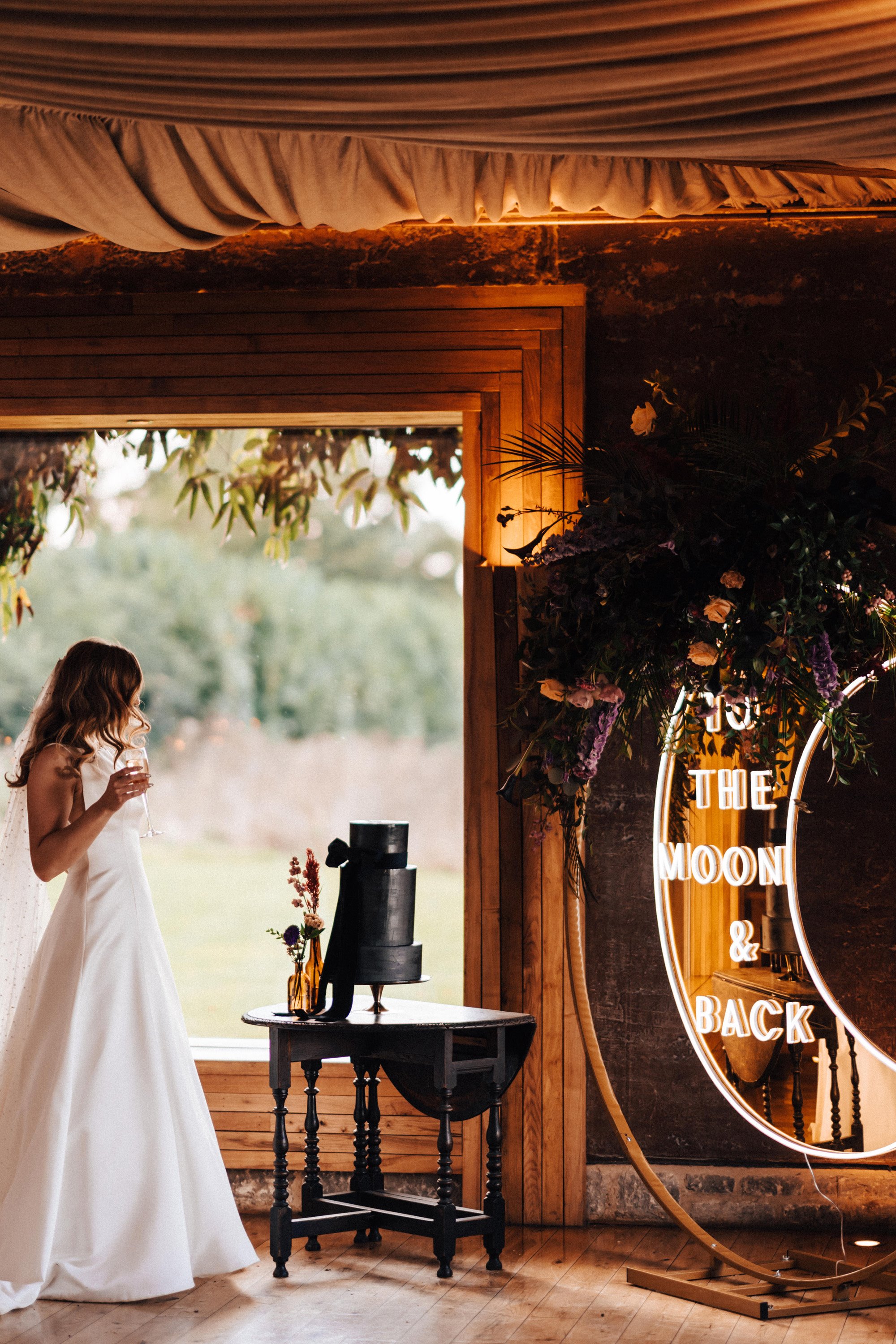 Bride sees her black wedding cake and crescent moon sign for the first time at her glamorous dark celestial autumn wedding reception in the cotswolds