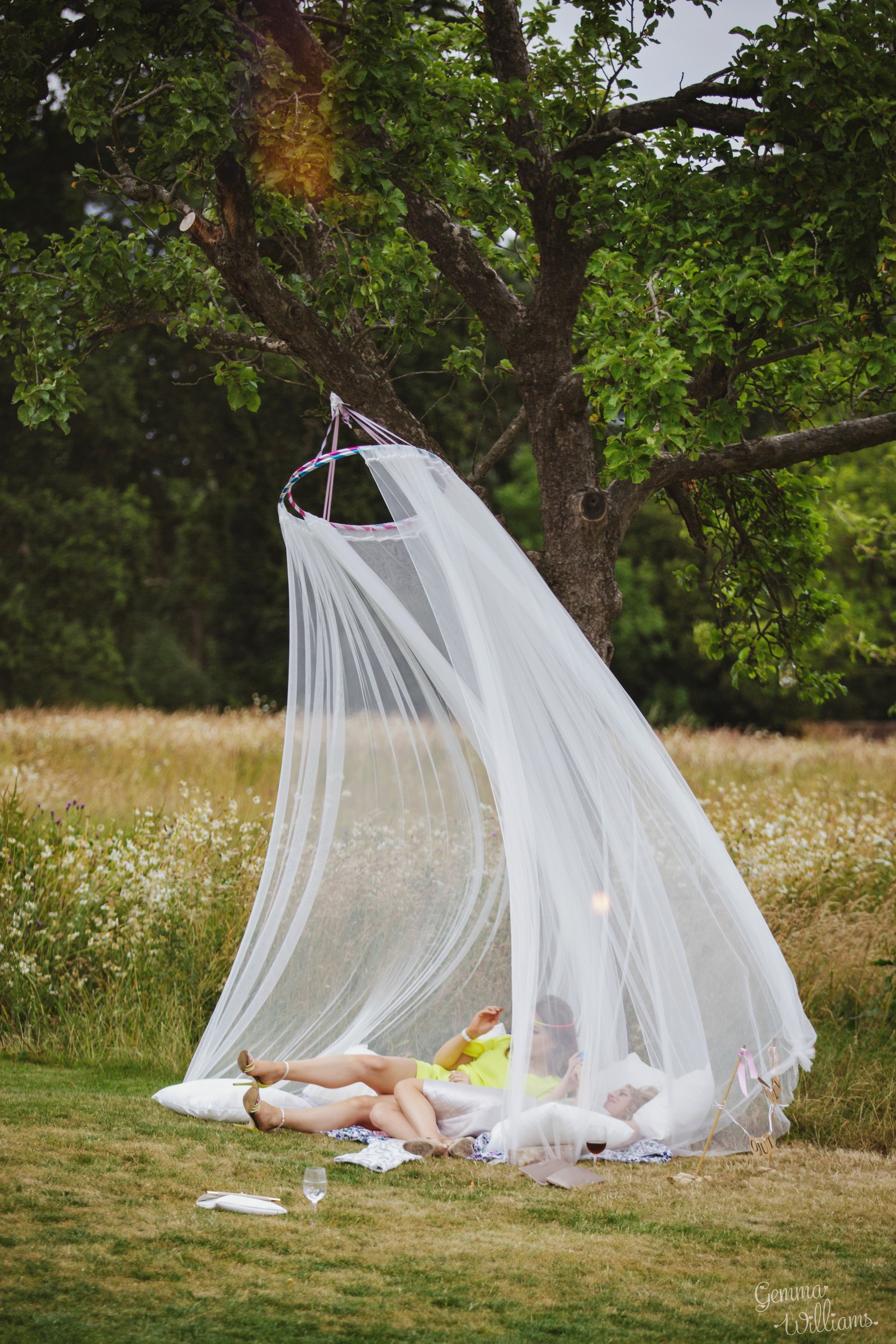 Guests chilling outside under a pretty mosquito net chill out seating area at an outdoor festival style wedding