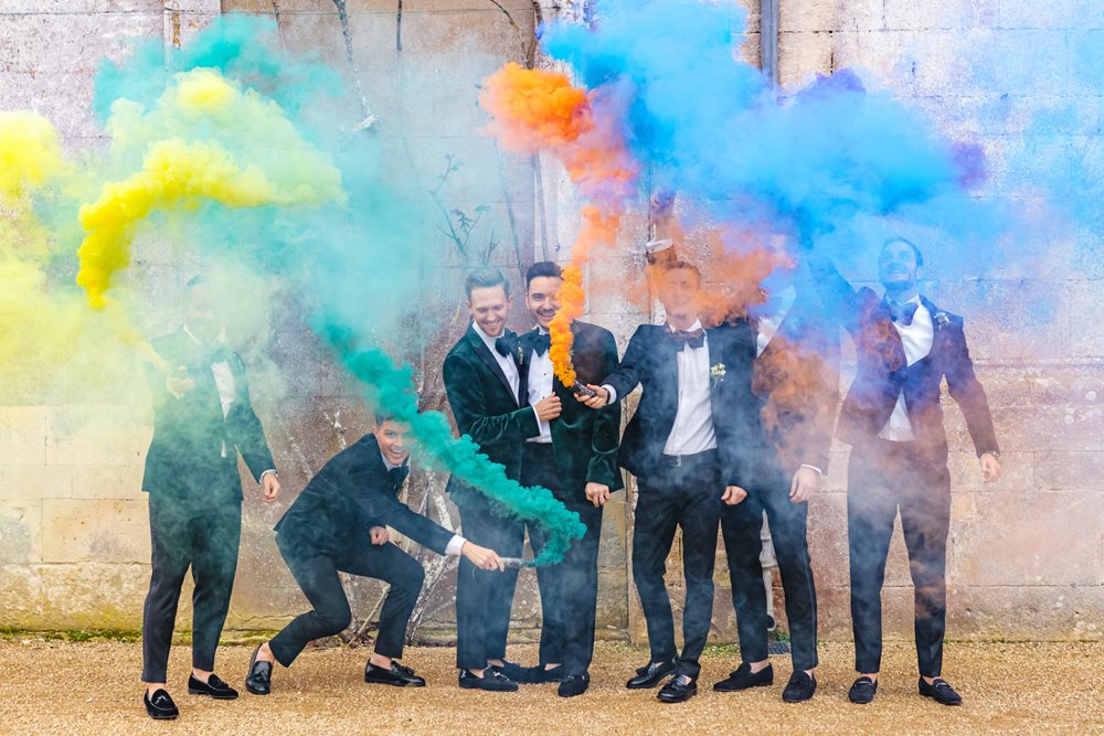 Rainbow smoke surrounds Grooms and groomsmen in tuxedos at their perfect gay wedding