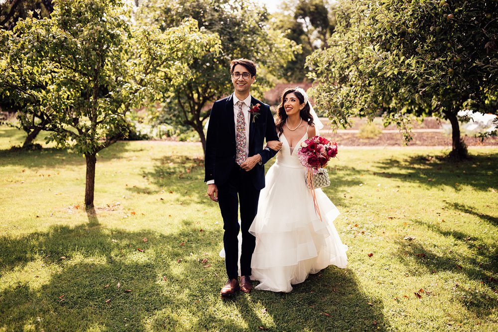 beautiful Couple walk through the orchard in the walled garden on their modern outdoor wedding day