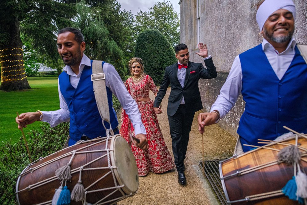 Indian newlywed couple dance behind dhol drummers leading way to their wedding reception