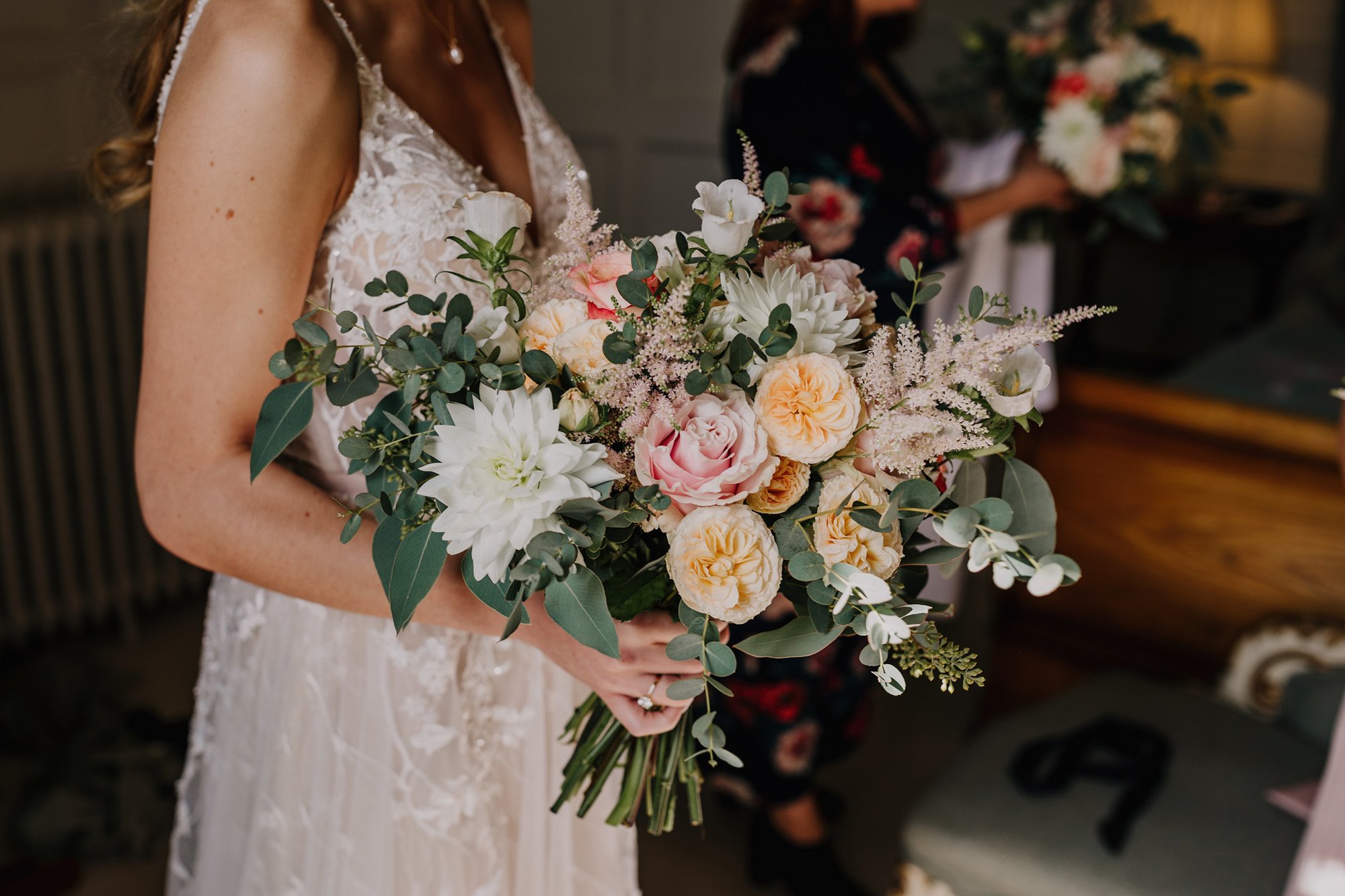 Bride in pearl necklace and pink lace wedding dress holding huge bouquet of pinks and greenery