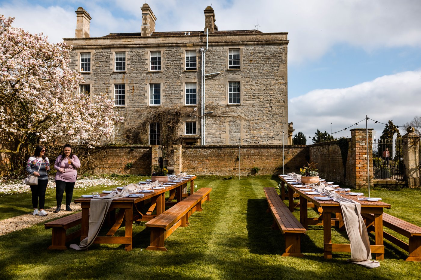 Outdoor wedding dining benches set up next to magnolia tree in the walled garden of stately home wedding venue Elmore Court for a wild wedding fair in 2022
