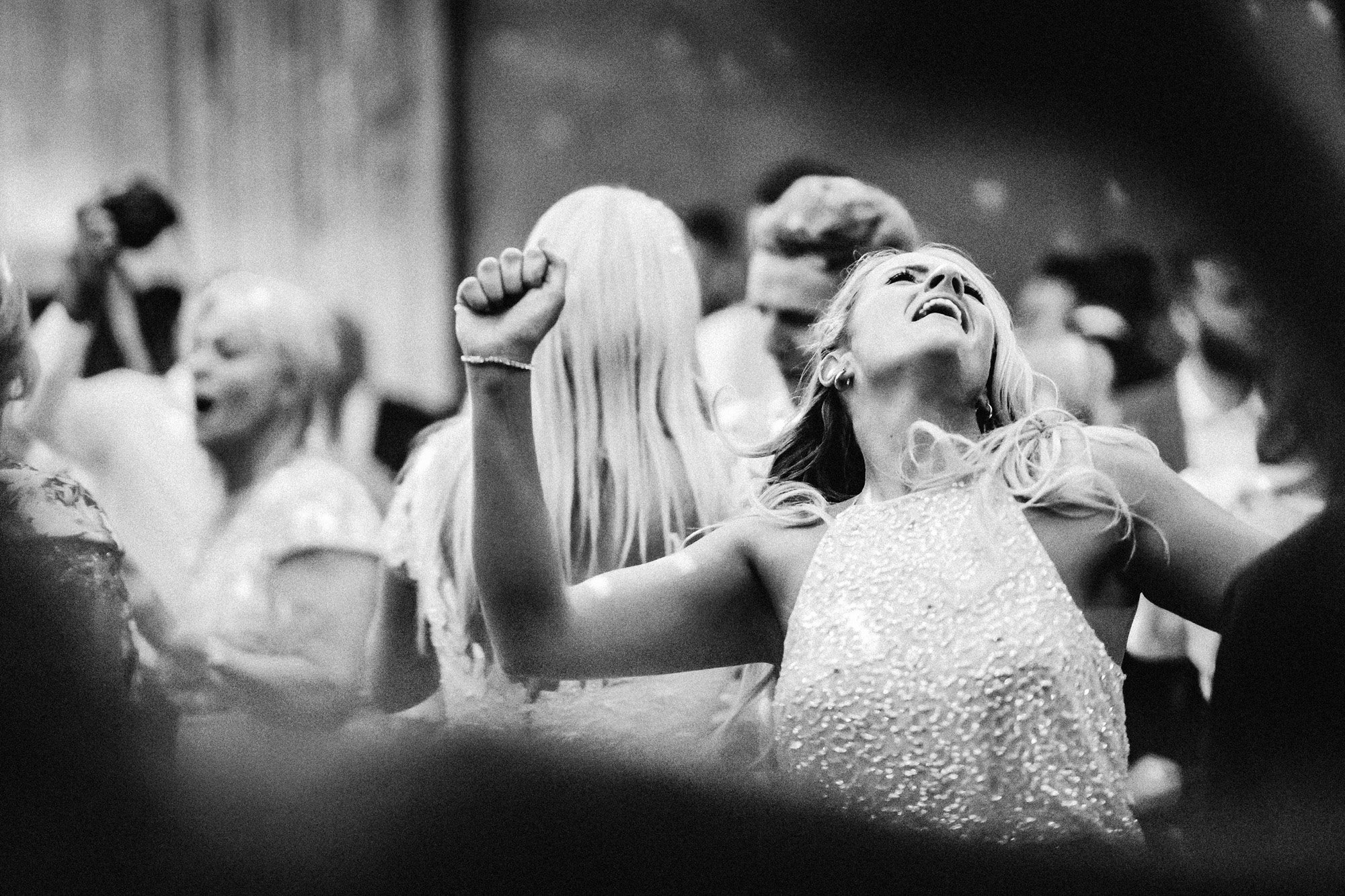 Bride dances with passion, throwing her head back with arms in the air in a candid black and white photo