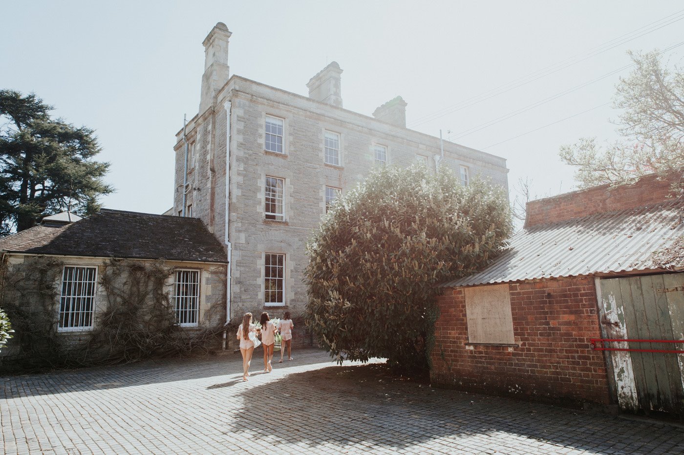 Bridesmaids in pyjamas walking towards Stately home Elmore Court in the hazy spring sunshine