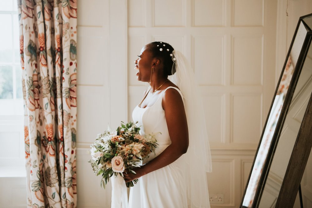 Beautiful modern lesbian bride in white wedding dress and pearls in her hair looks so happy to see her bride coming towards her