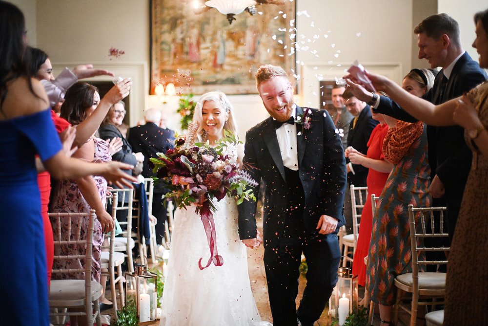 autumnal wedding ceremony bride and groom walking down aisle with confetti