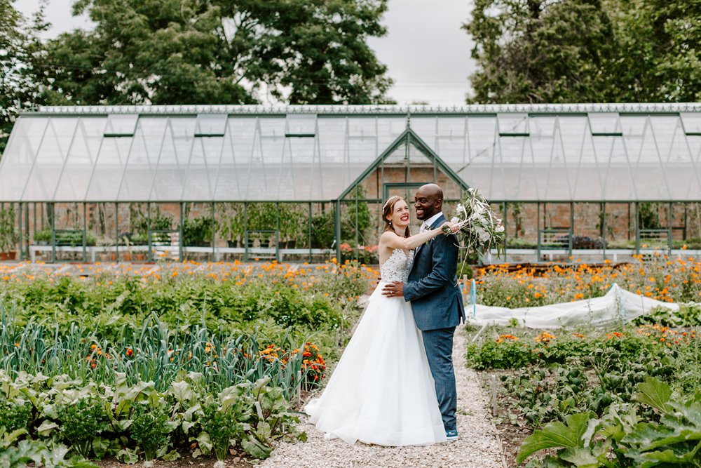 Couple pose in front of green house at walled garden wedding