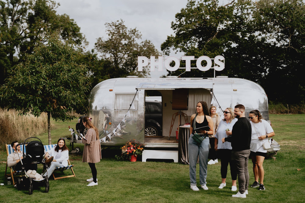 Cool silver trailer caravan photo booth with pink neon lights and bunting at unusual wedding venue elmore court