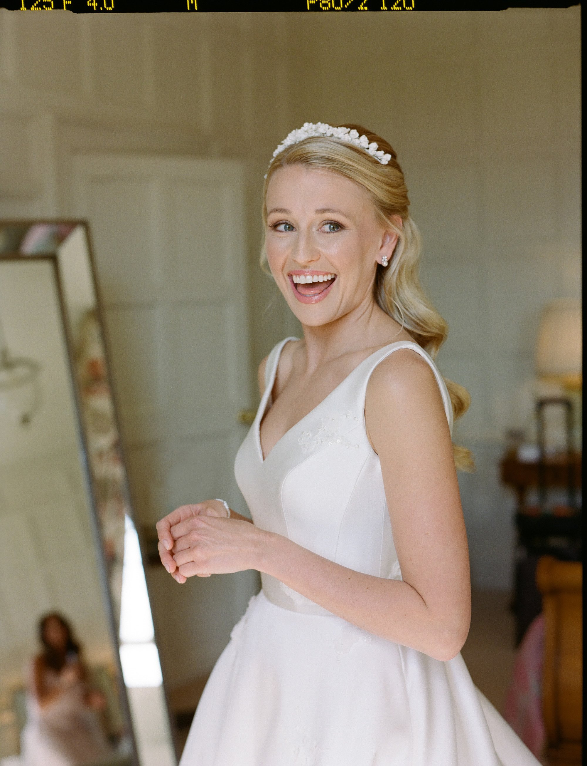 Elegant bride in simple satin dress with full skirt, pearl tiara and pearl earrings smiles on her wedding day at luxury Cotswolds wedding venue Elmore Court