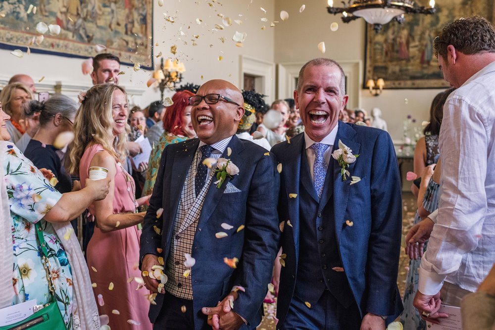Very happy newlywed gay couple smile and laugh with confetti all over mansion house elmore court