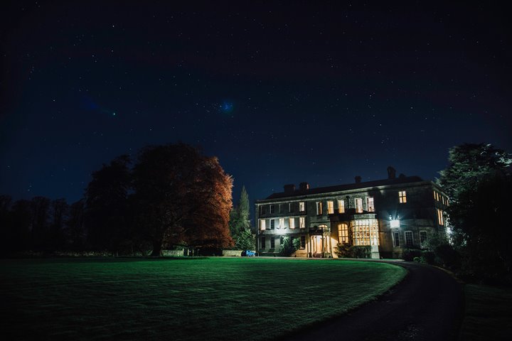 Glowing stately home Elmore Court at night. The huge beech tree to the left of the grade two listed house is slightly lit up by the light from the windows