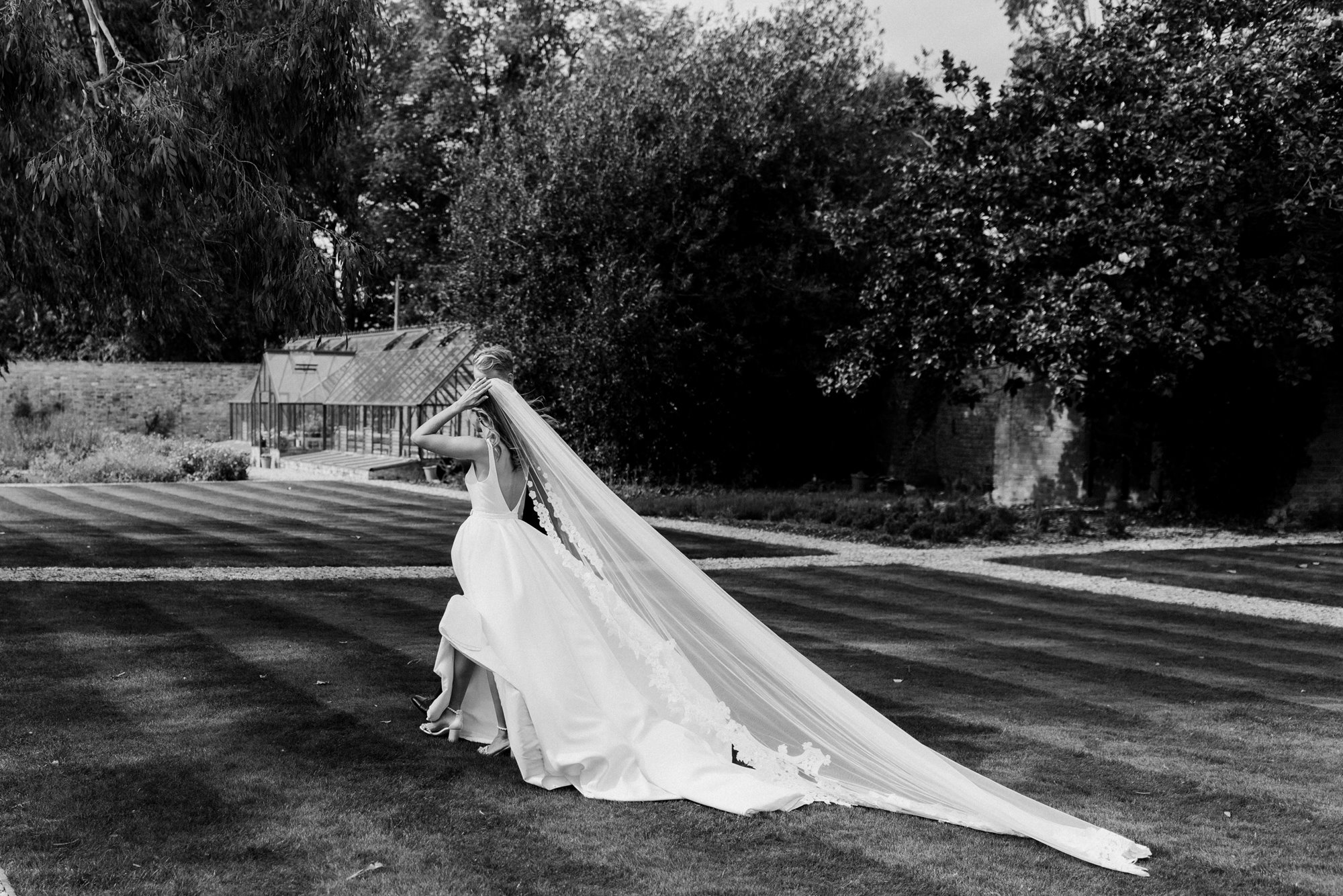 bride in long romantic veil walking through a walled garden of a stately home in gloucsteshire
