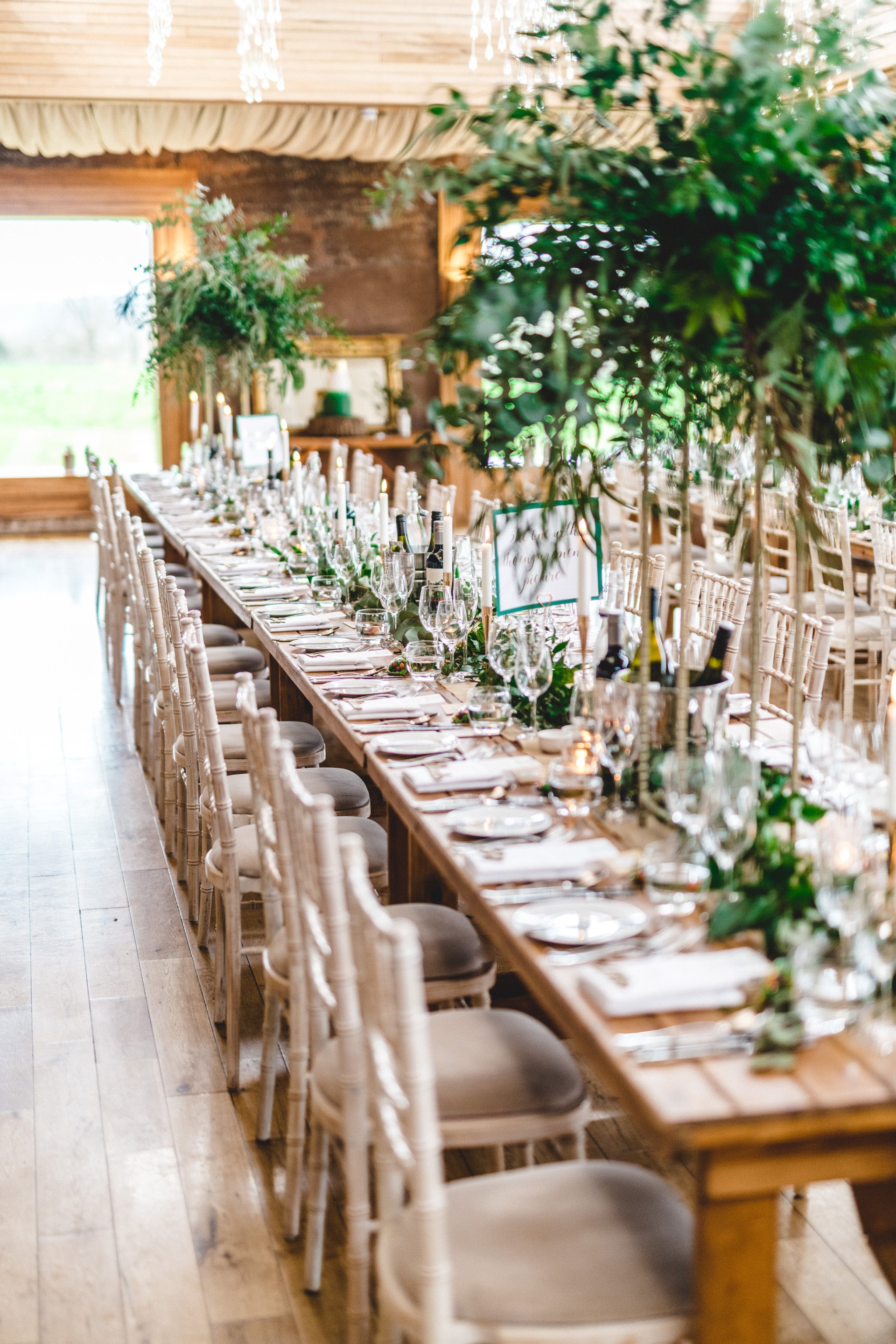 Long wooden tables with greenery in a light and airy reception at a gay wedding venue in the UK