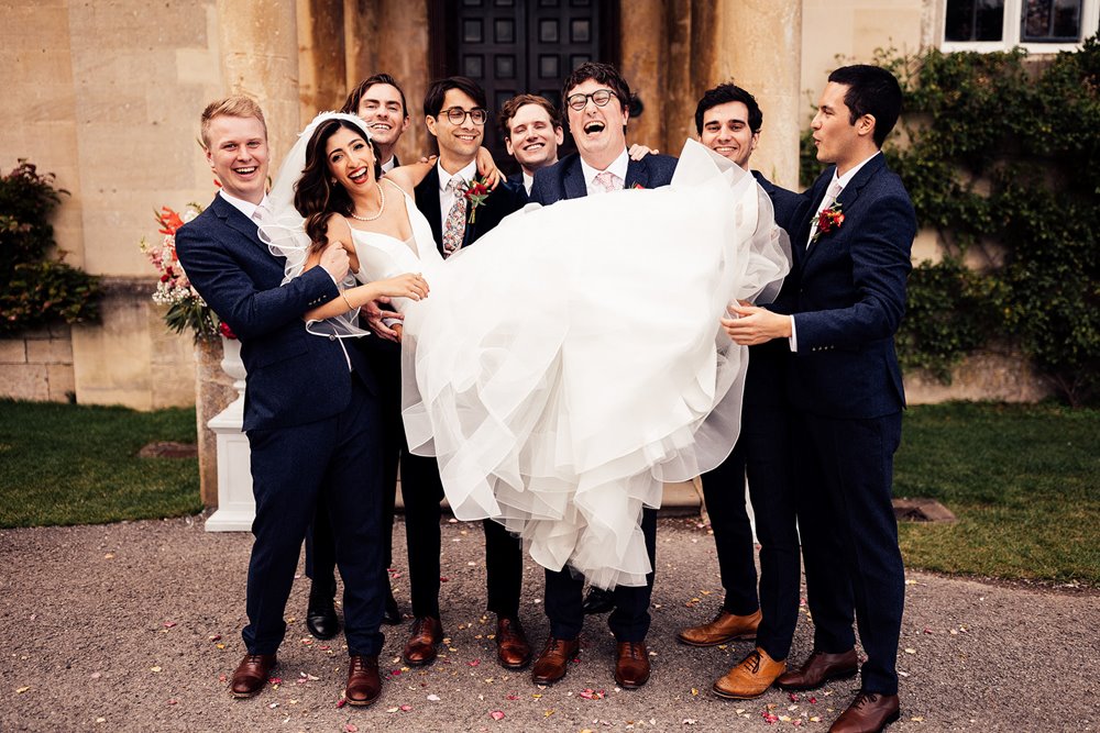 Groomsmen hold bride in fun wedding photo outside mansion house elmore court in the cotswolds