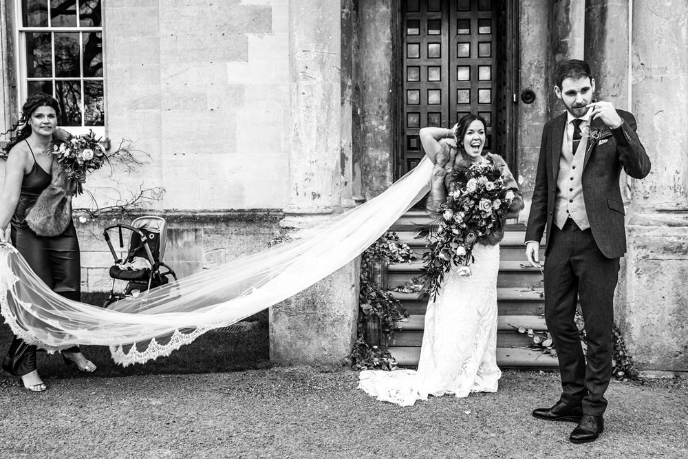 Bride happily surprised wearing long cathedral length veil in front of weekend wedding venue