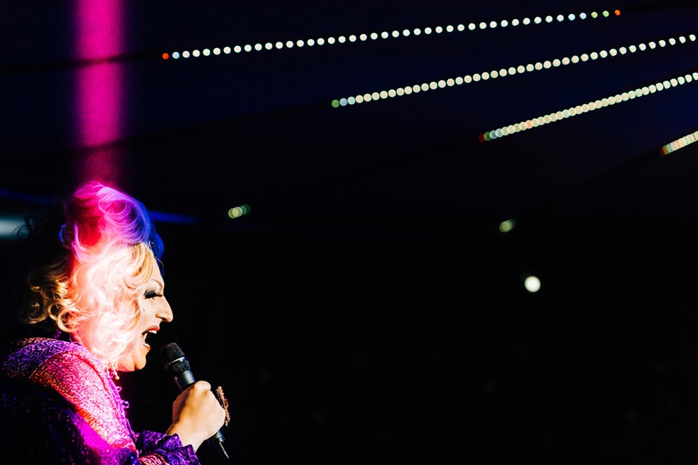 Drag queen brightly lit up in pink and white light on stage at elmore court's special pop up covid cabaret the parrot cage