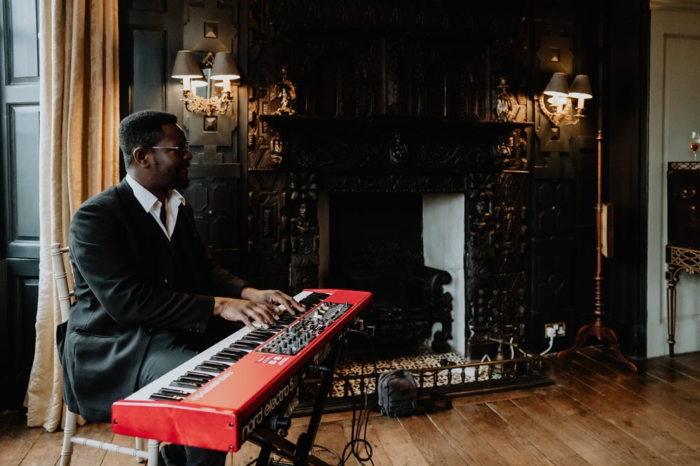 A musician playing a bright red keyboard next to an impressive fireplace at a reception at Elmore Court