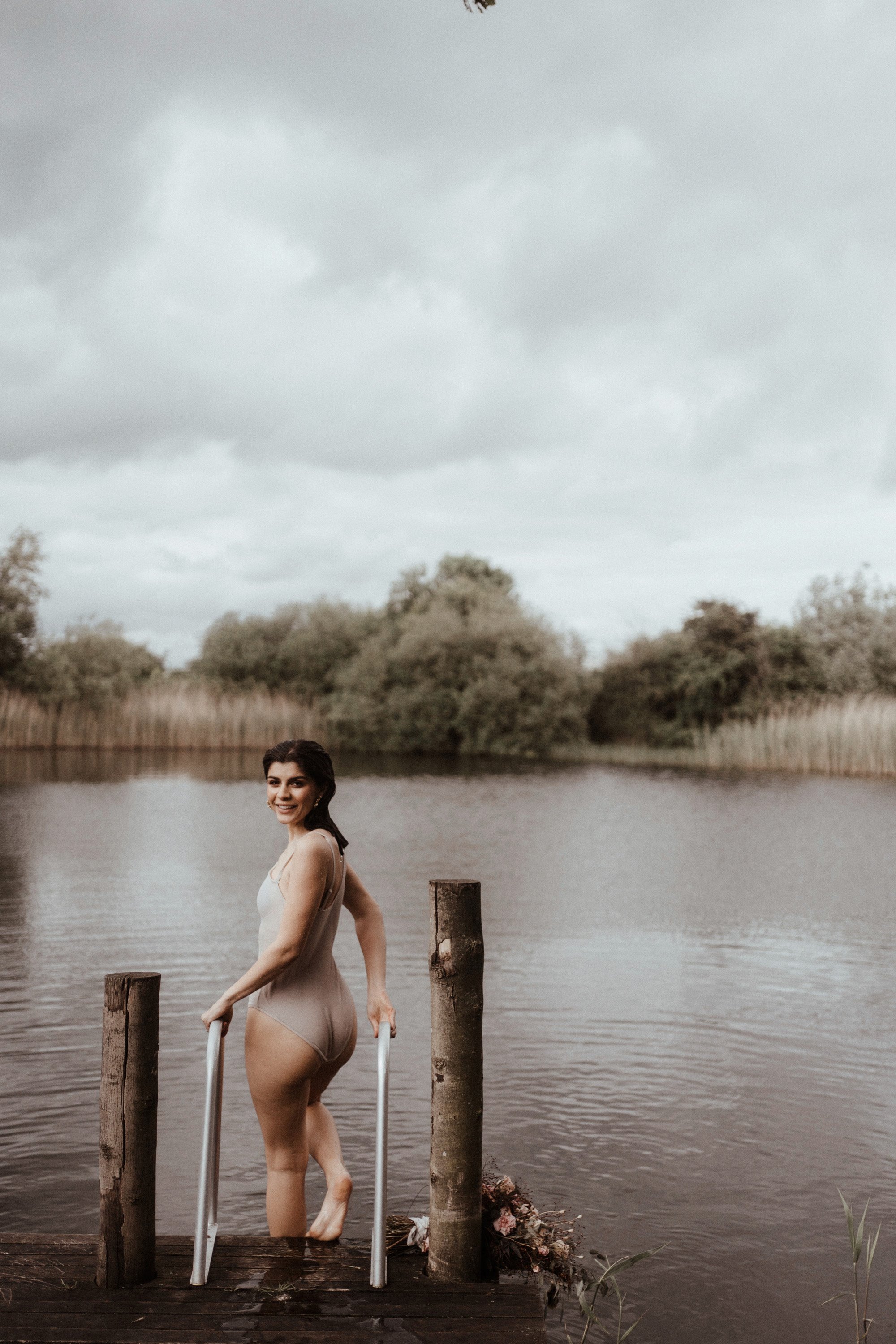 Bride getting in the lake for a wild swim before wedding at stately home elmore court in the Cotswolds countryside