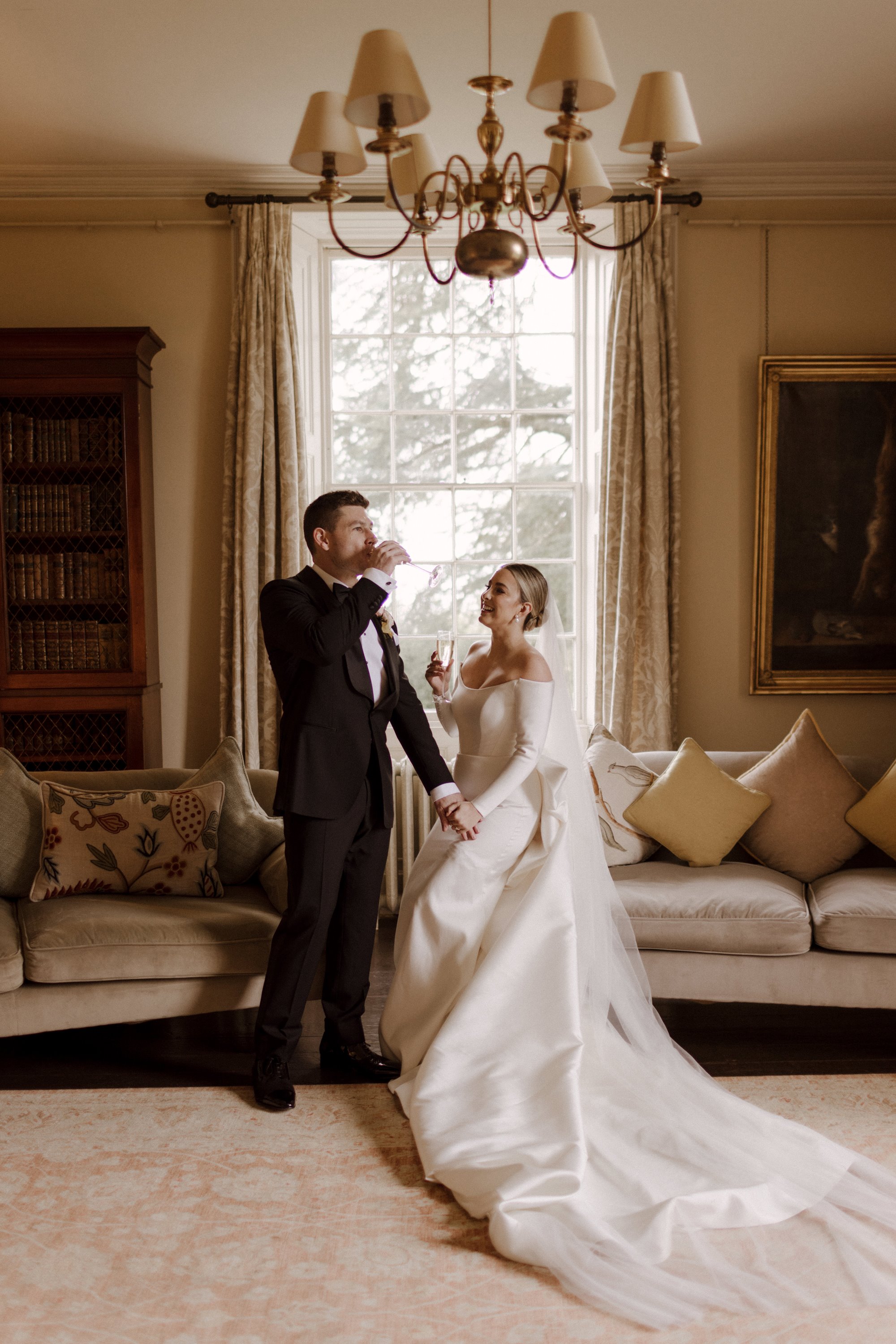 Bride and groom enjoying a glass of bubbles in an elegant room of a stately home in the Cotswolds