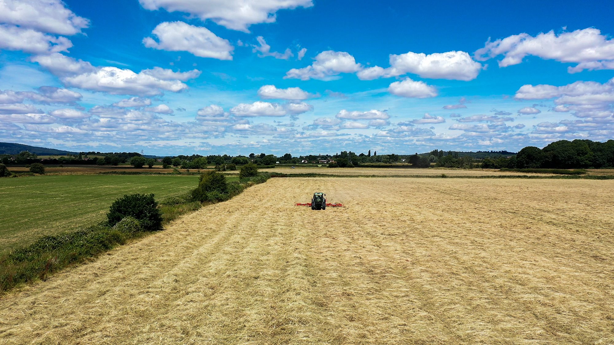 A tractor mowing a field on a beautifully sunny day with a bright blue sky and wispy clouds