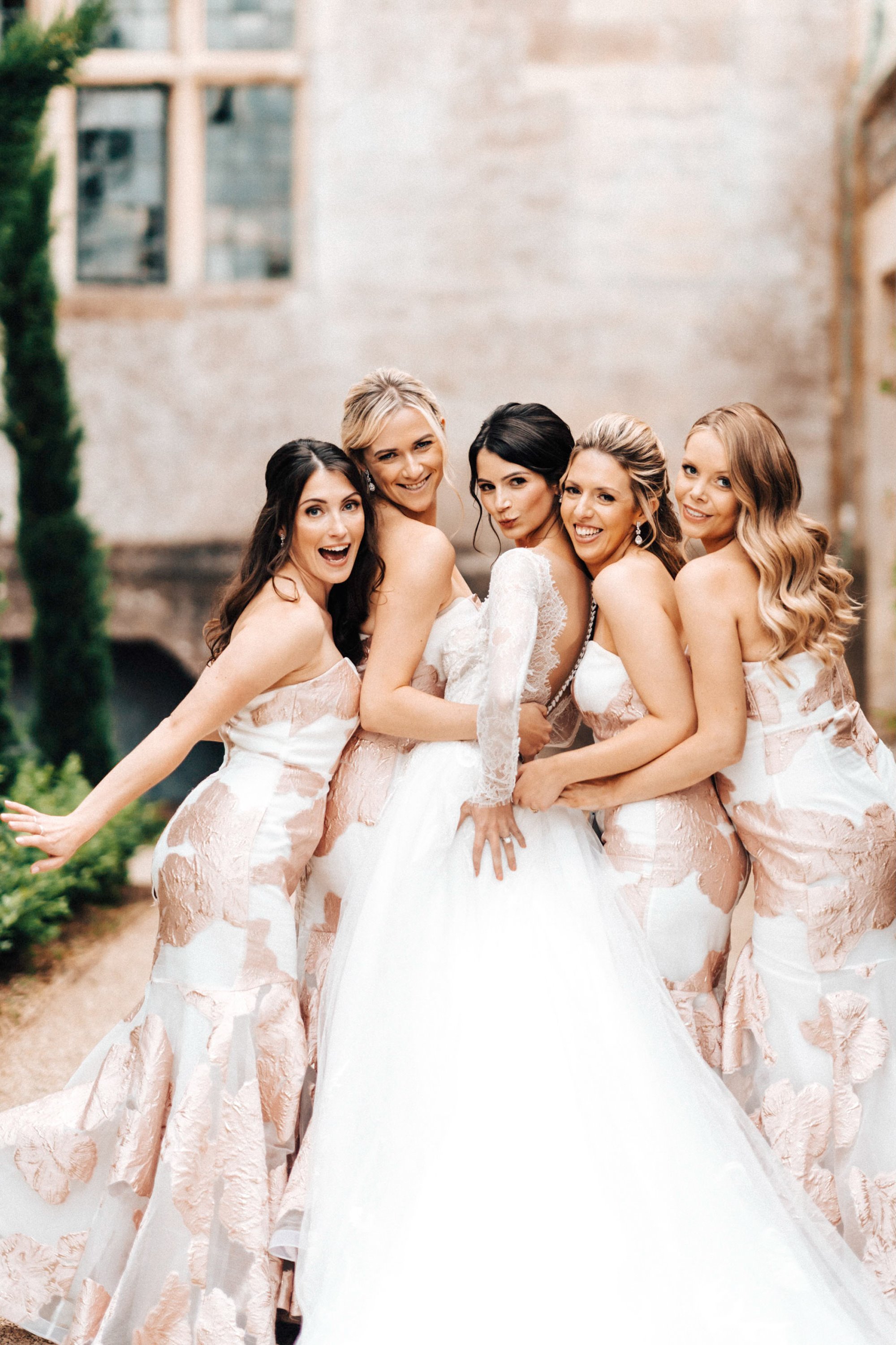 Bride with bridesmaids in pink and white patterned dresses pose outside mansion house wedding venue
