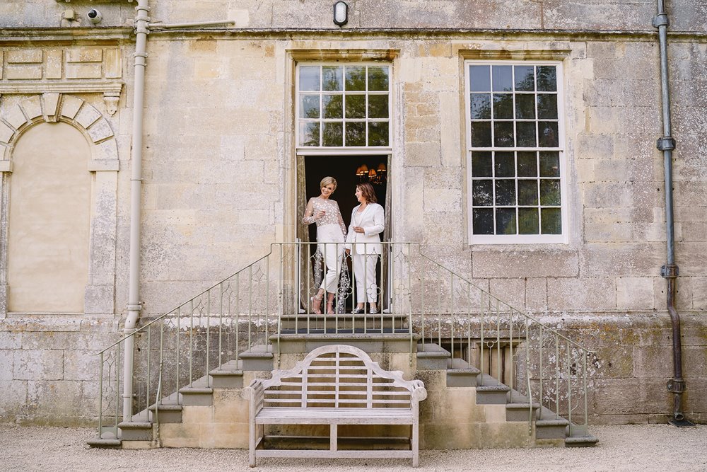 Two brides stand on steps of their wedding venue