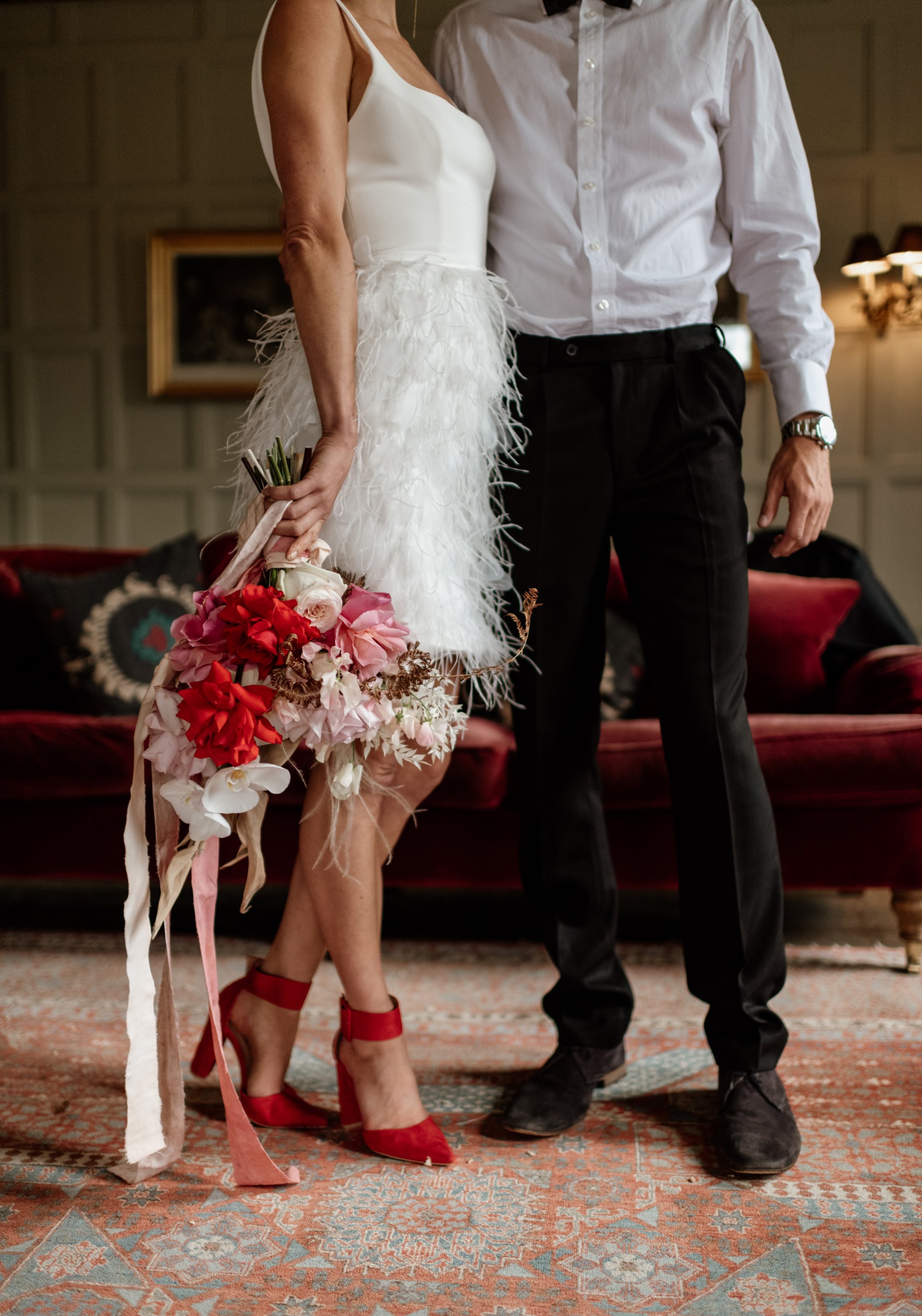 Bride and groom posing for a red and white themed wedding, with bright red high heels and a bouquet of red flowers