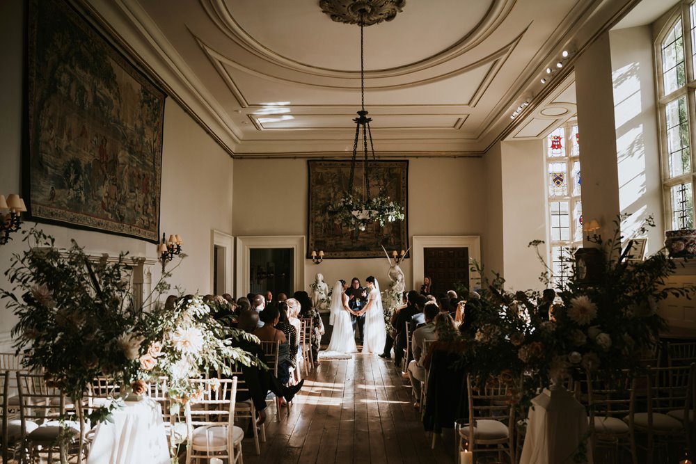 Two brides look like something from a fairytale wearing white wedding dresses and veils in magical stately home ceremony
