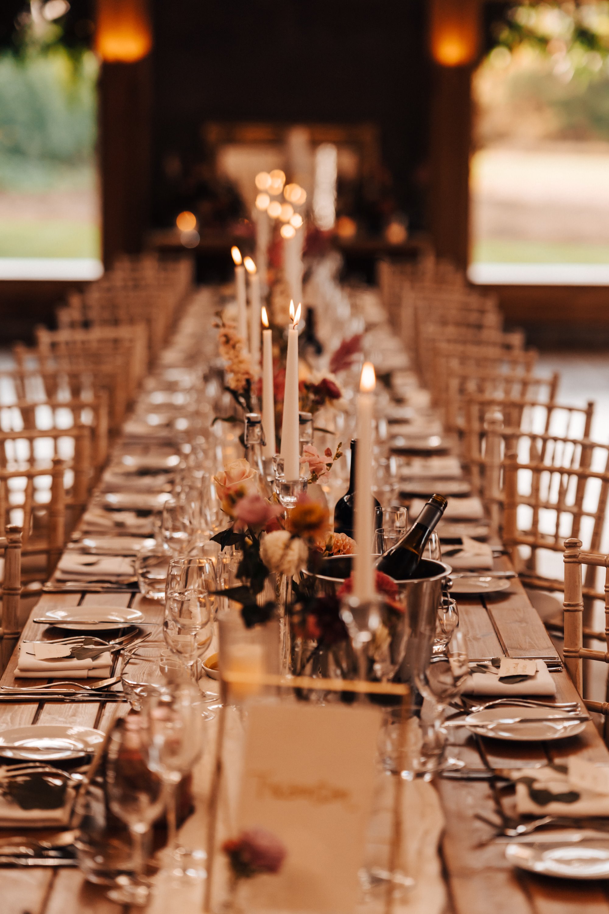 tall candles flicker on a long wedding reception table, decorated with pink and white flowers