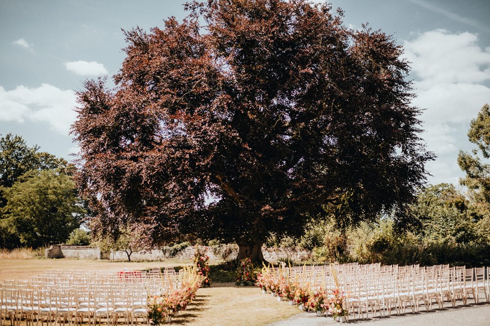 outdoor wedding ceremony next to a magnificent tree on the lawn of stately home