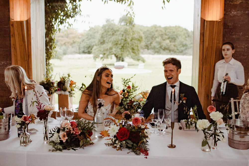 Bride wearing crown sitting next to her groom at their modern autumnal wedding reception