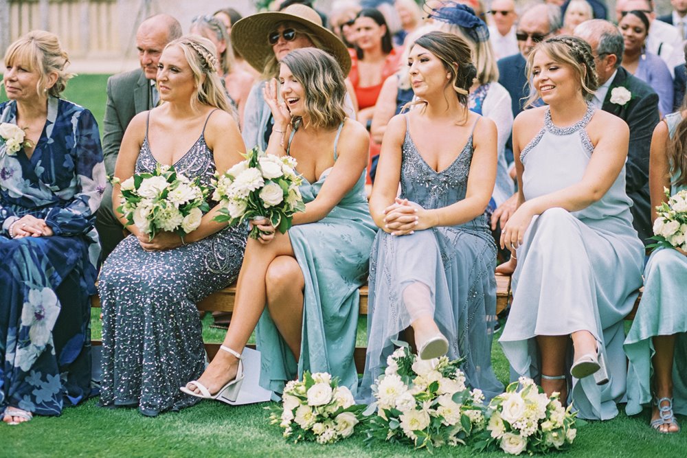 Outdoor wedding inspiration mismatched green hue bridesmaids sit and watch the outdoor ceremony