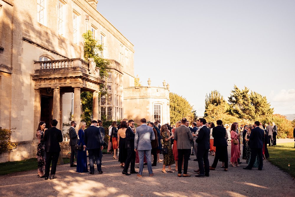 wedding guests enjoy sunny drinks reception outside mansion house wedding venue in the cotswolds