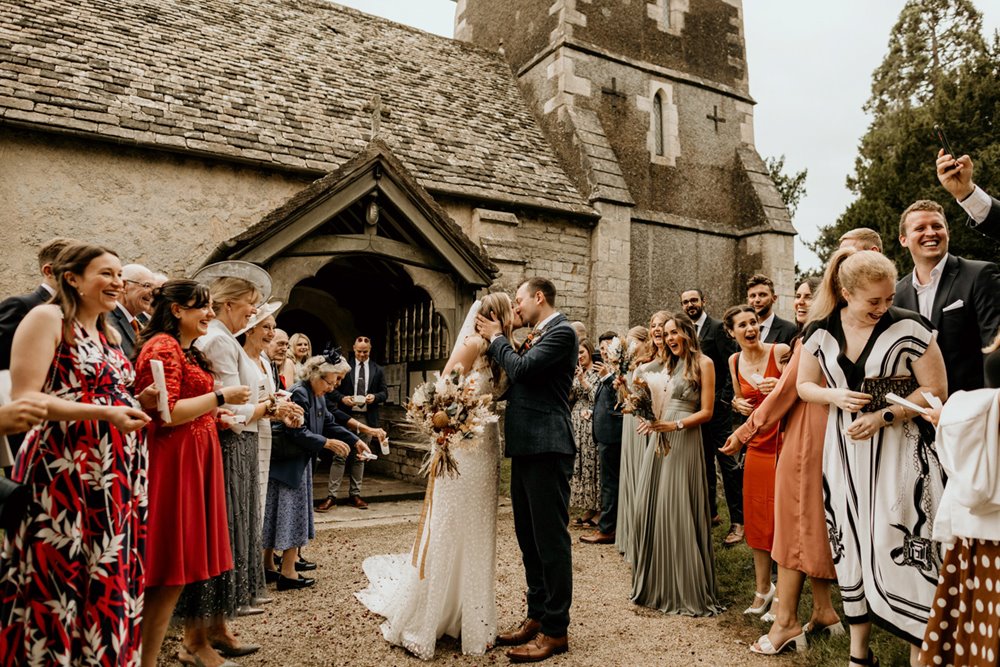 Just married Bride and groom kiss outside prettiest church in England- Elmore in Gloucestershire