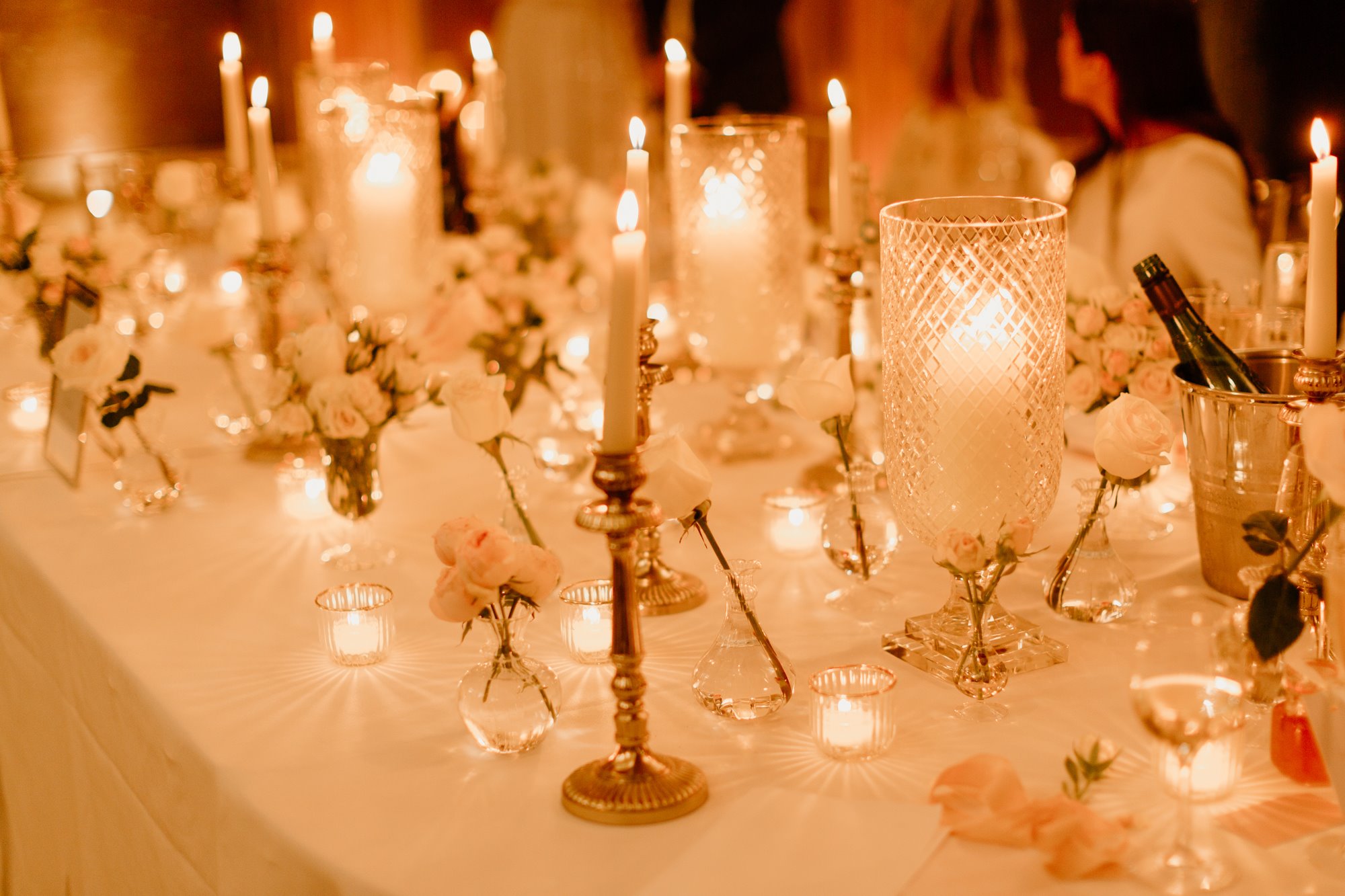 twinkling tea lights lighting up a wedding table with small vases of pink flowers and coolers of wine